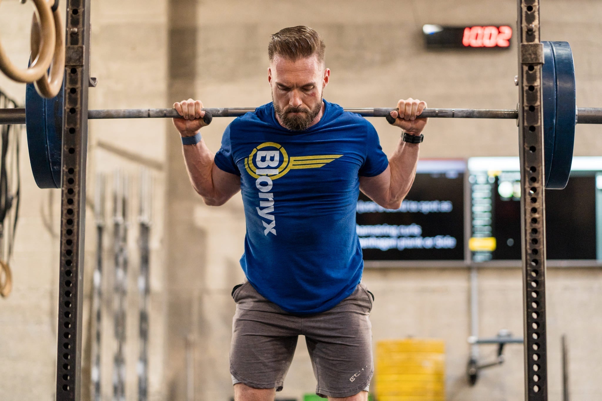 A man performs a heavy barbell squat in a gym wearing a Blonyx t-shirt.