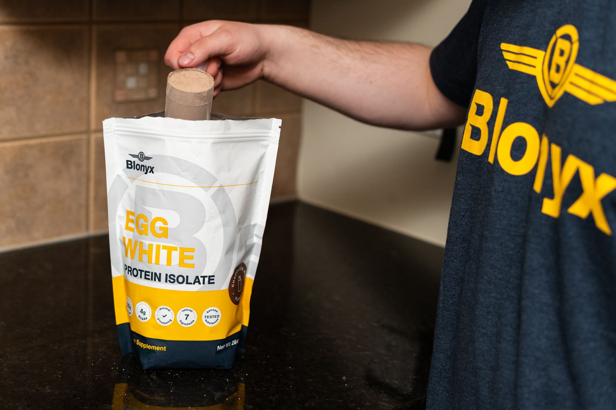 A person scoops Blonyx Egg White Protein Isolate powder from the pouch