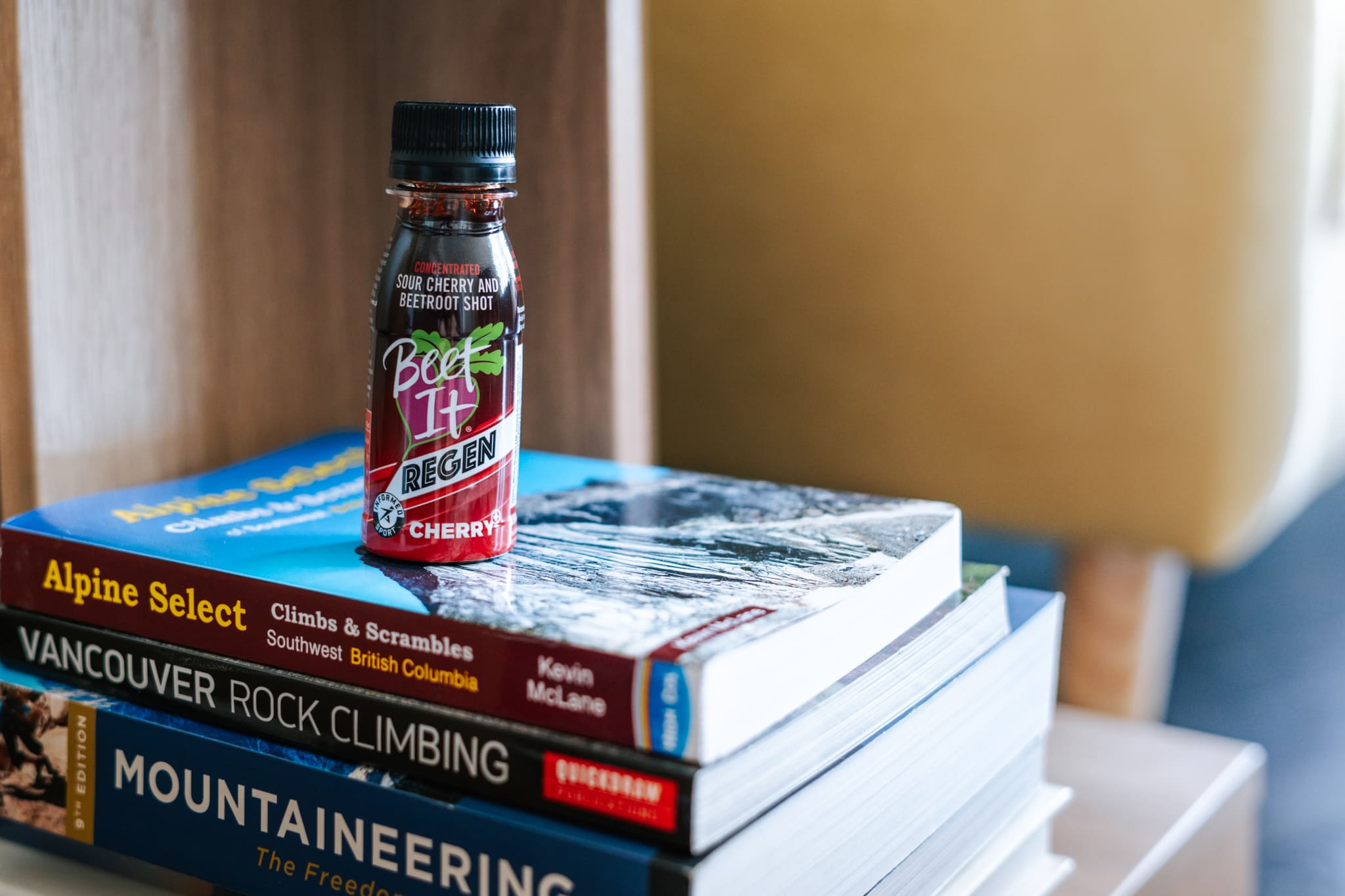 A Beet It Regen Cherry+ Shot Sits On Top of a Stack of Climbing and Mountaineering Books