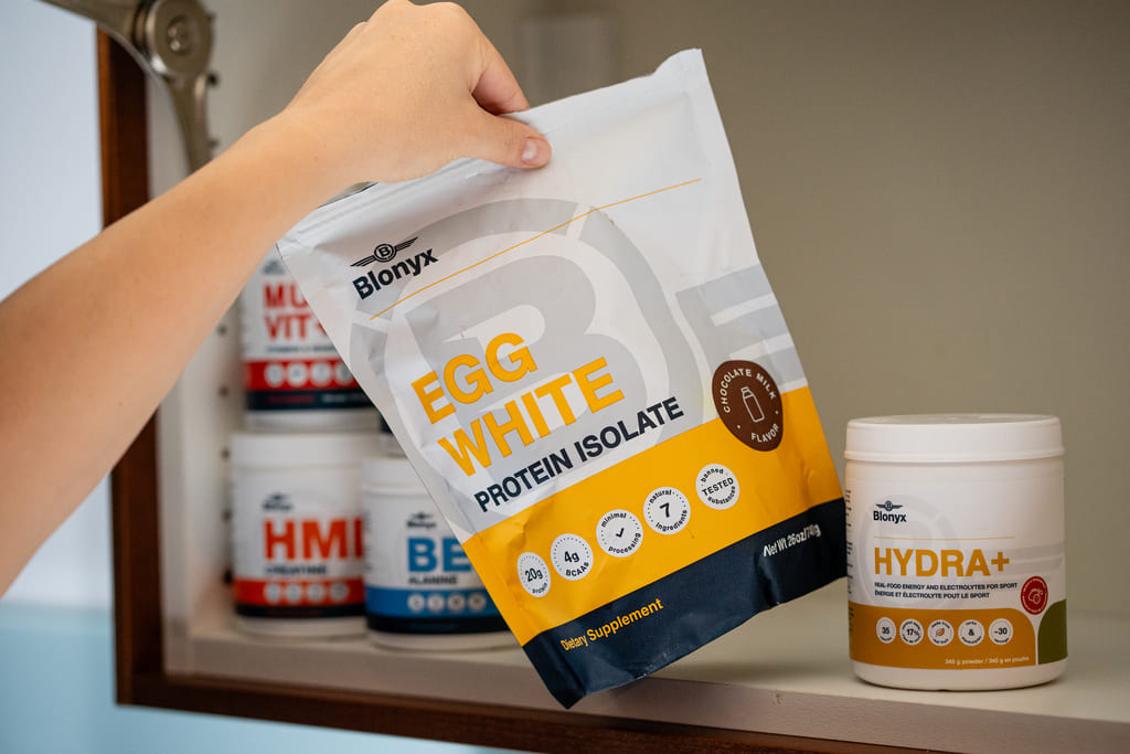 Person holding a Bionyk Egg White Protein Isolate package with other supplement containers on a shelf.