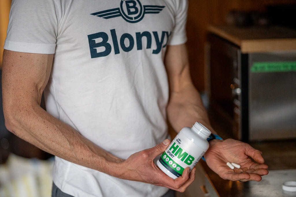 Person holding a Blonyx HMB Sport bottle  wearing a white t-shirt with 'Blonyx'.