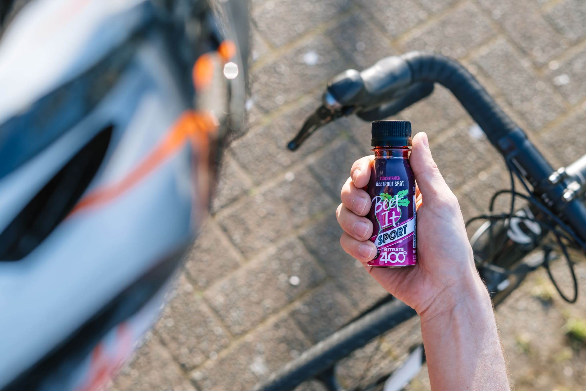 Cyclist looking down at a Beet It Sport Nitrate 400 shot they're holding