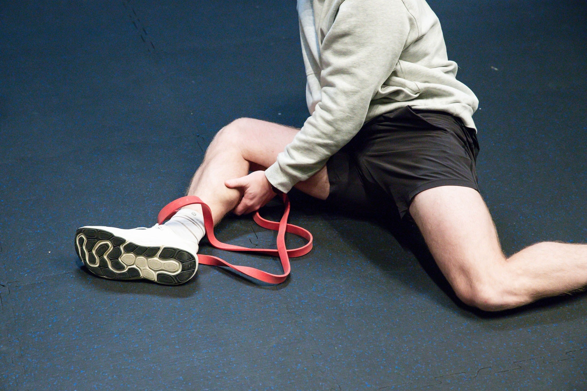 Athlete stretching on the gym floor using a resistance band around their ankle.