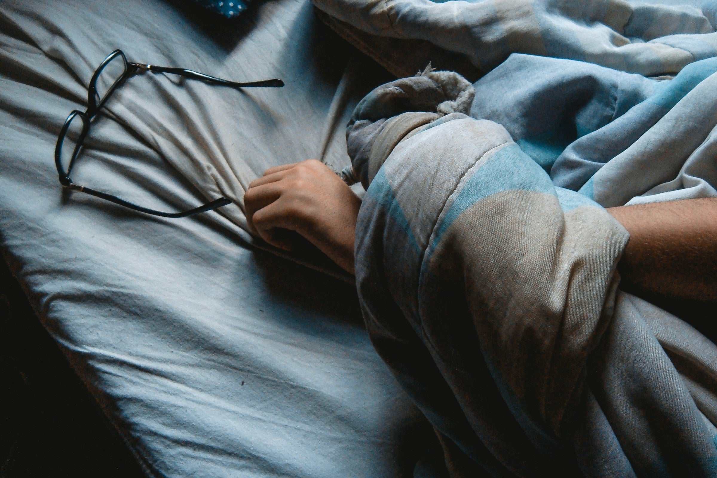 An athlete's glasses and arm poking out from under the covers on their bed