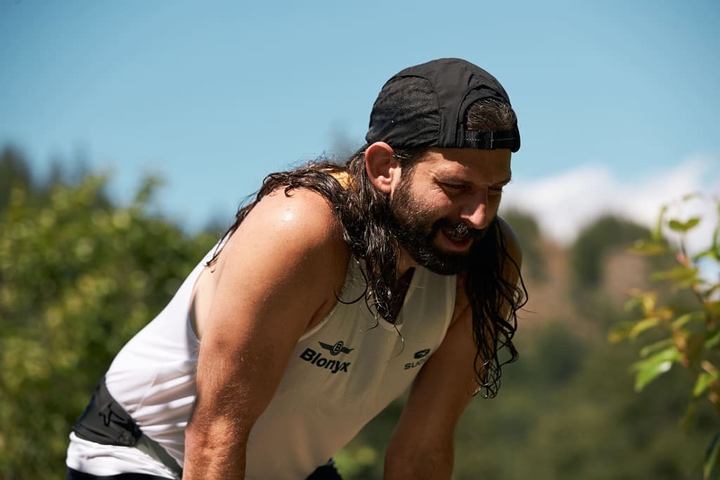 Man outdoors wearing a white tank top with a Blonyx logo, surrounded by greenery.