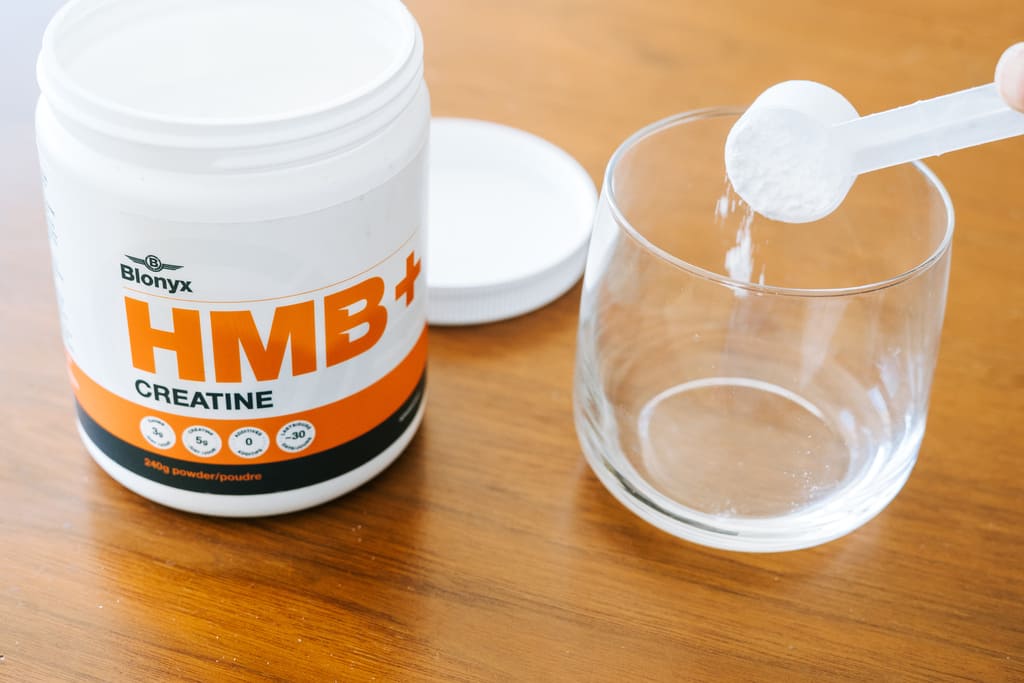 Blonyx HMB+ Creatine container with a glass on a wooden surface