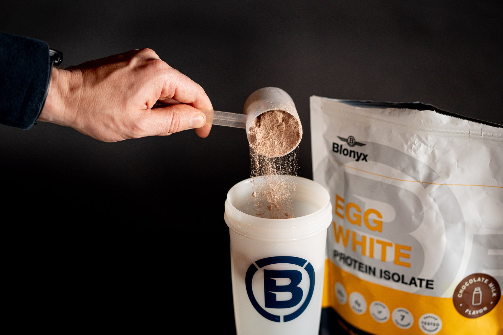 Scooping Blonyx Egg White Protein Isolate into a shaker bottle