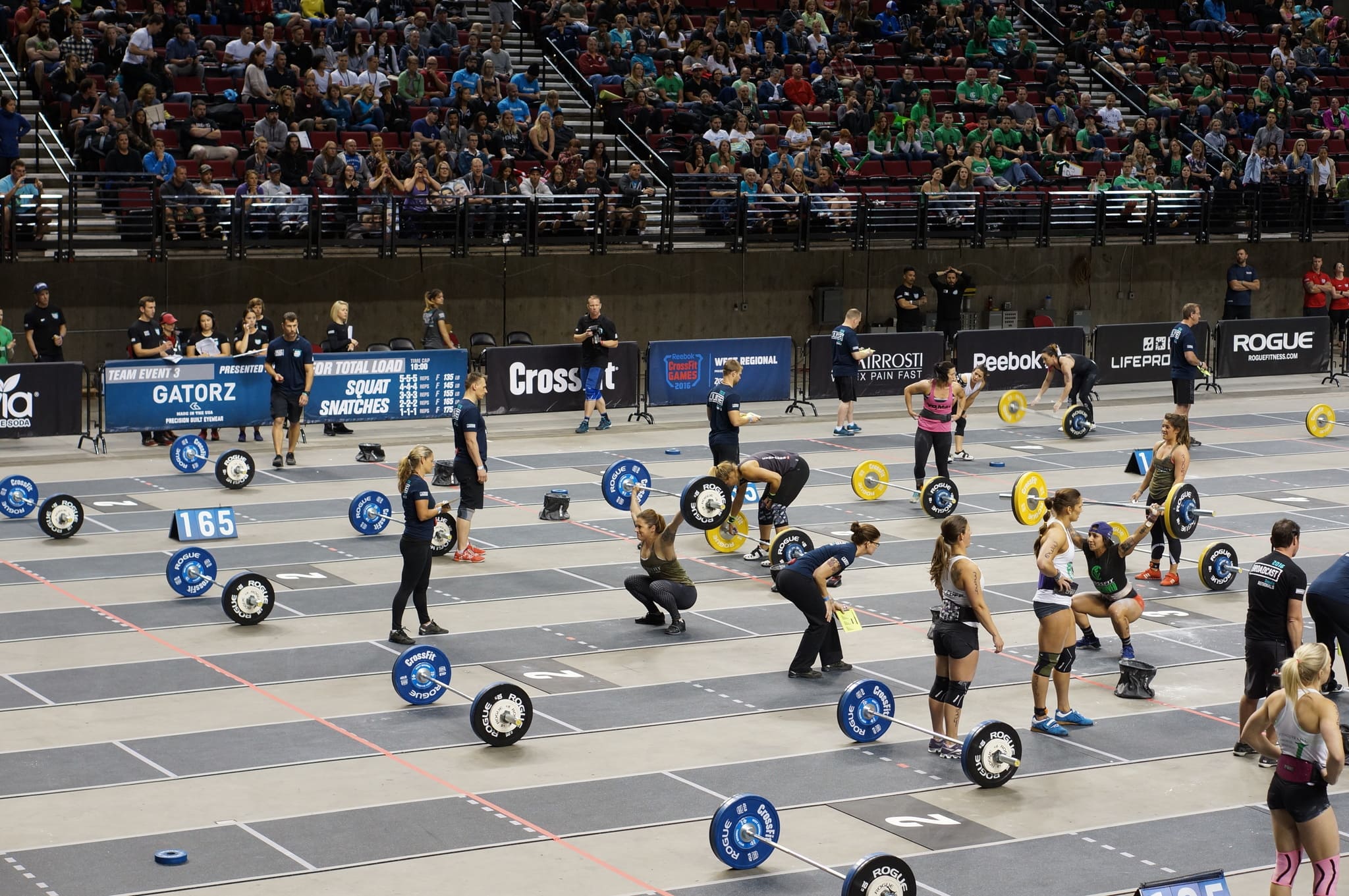 Athletes lifting barbells in a weightlifting competition with spectators in the background.
