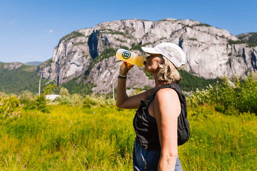 Person drinkingBlonyx  Hydra+ from a Blonyx water bottle with a mountainous landscape in the background