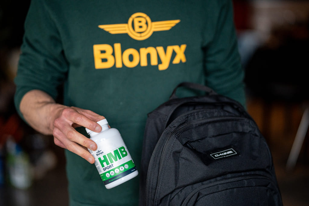 Person wearing a green 'Blonyx' shirt taking HMB Sport Out of a Backpack