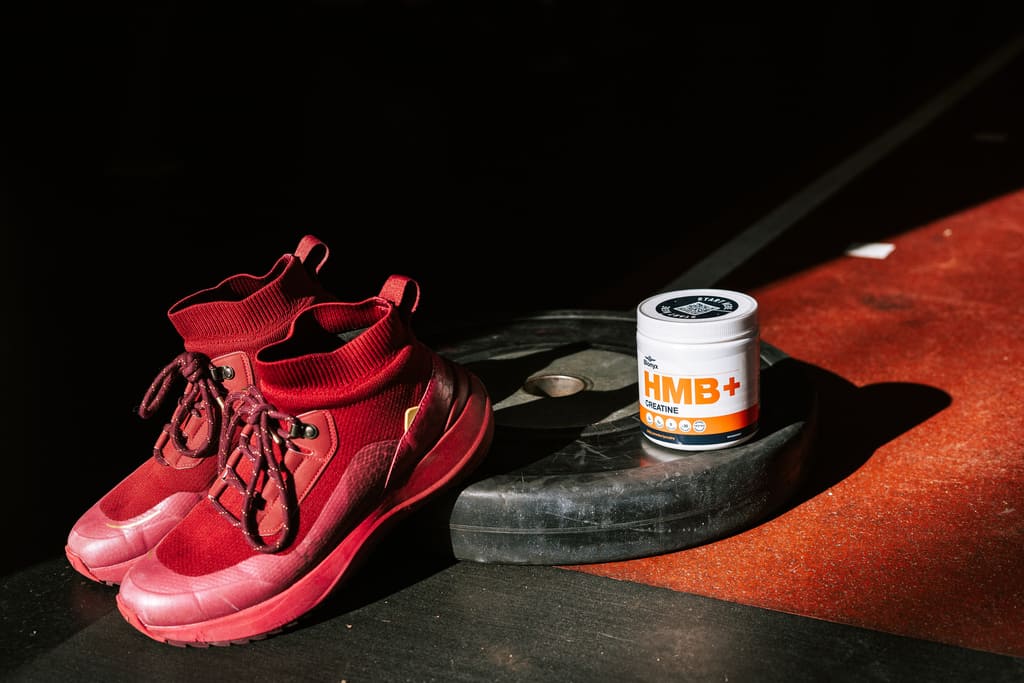 Red athletic shoes and a container of Blonyx 'HMB+ Creatine' on a gym floor.