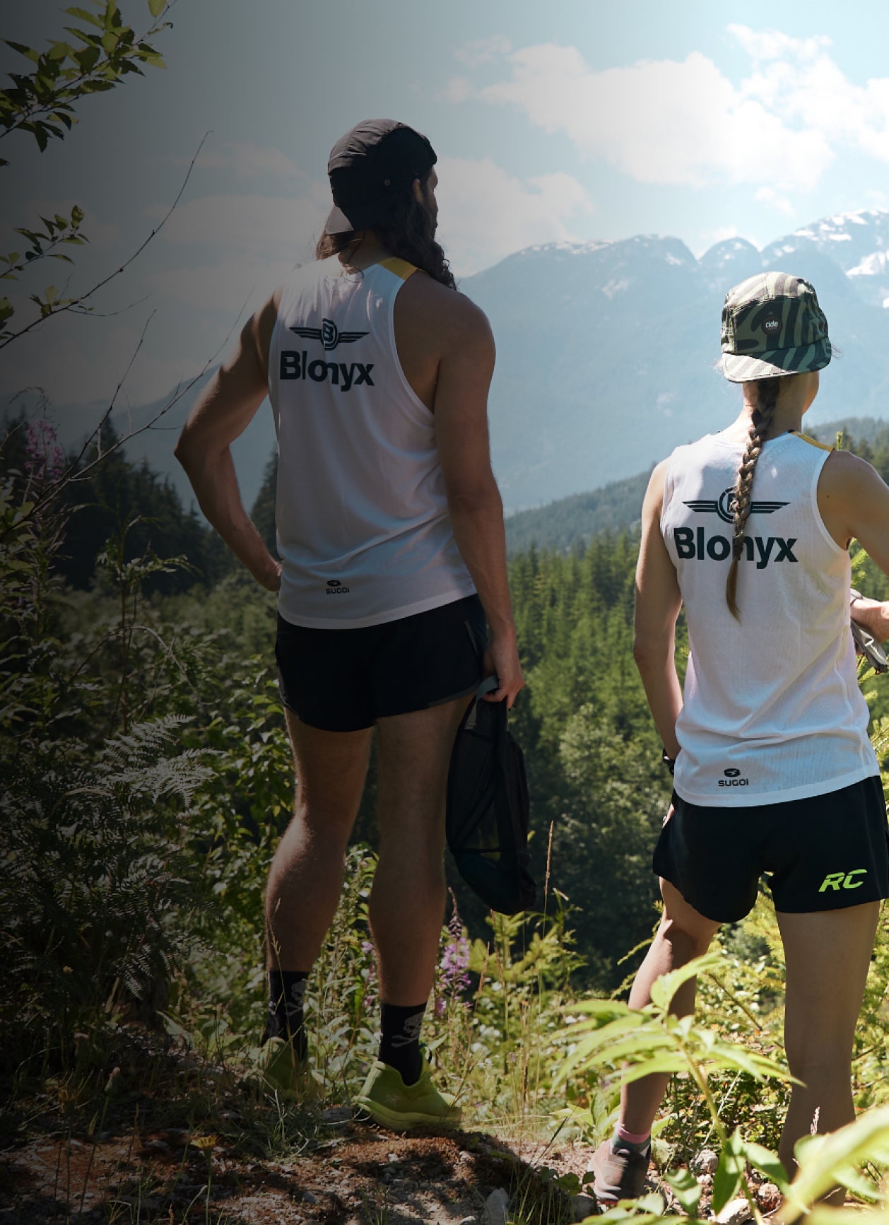Two trail runners wearing Blonyx jerseys sand standing at the top of a mountain looking at the view