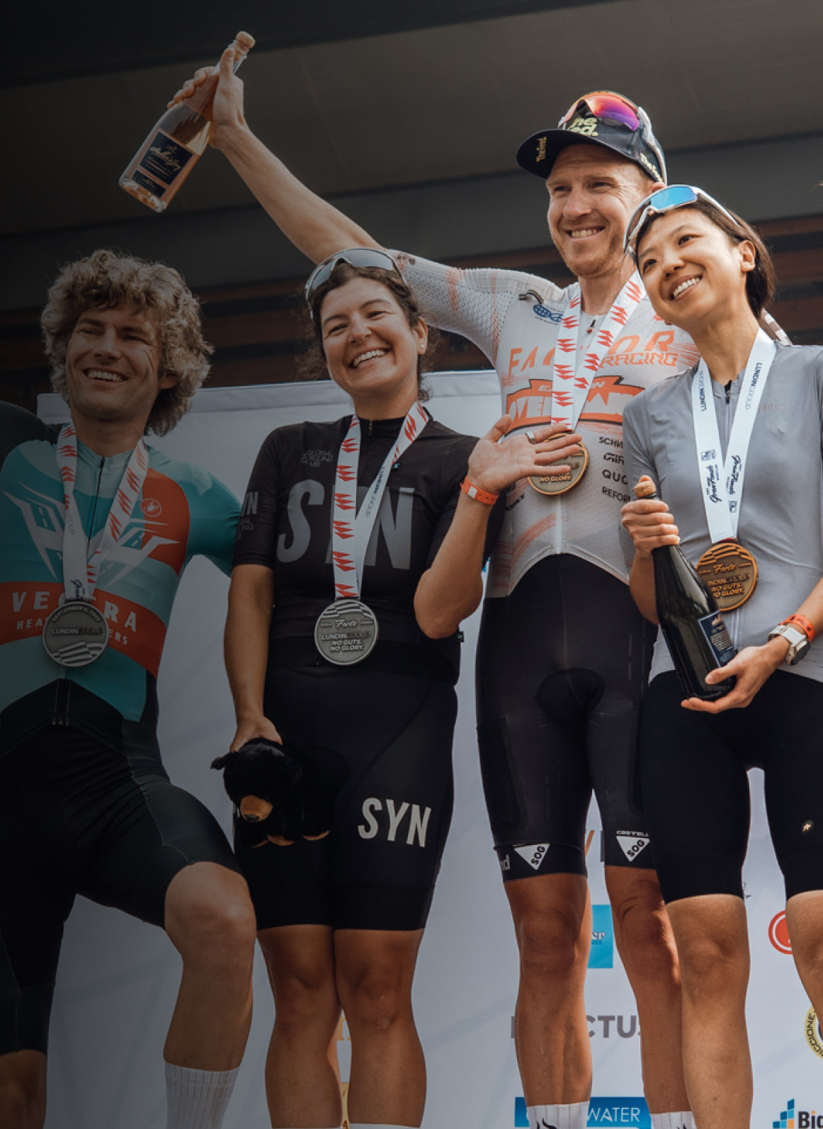 Group of cyclists celebrating on a podium with medals and bottles.