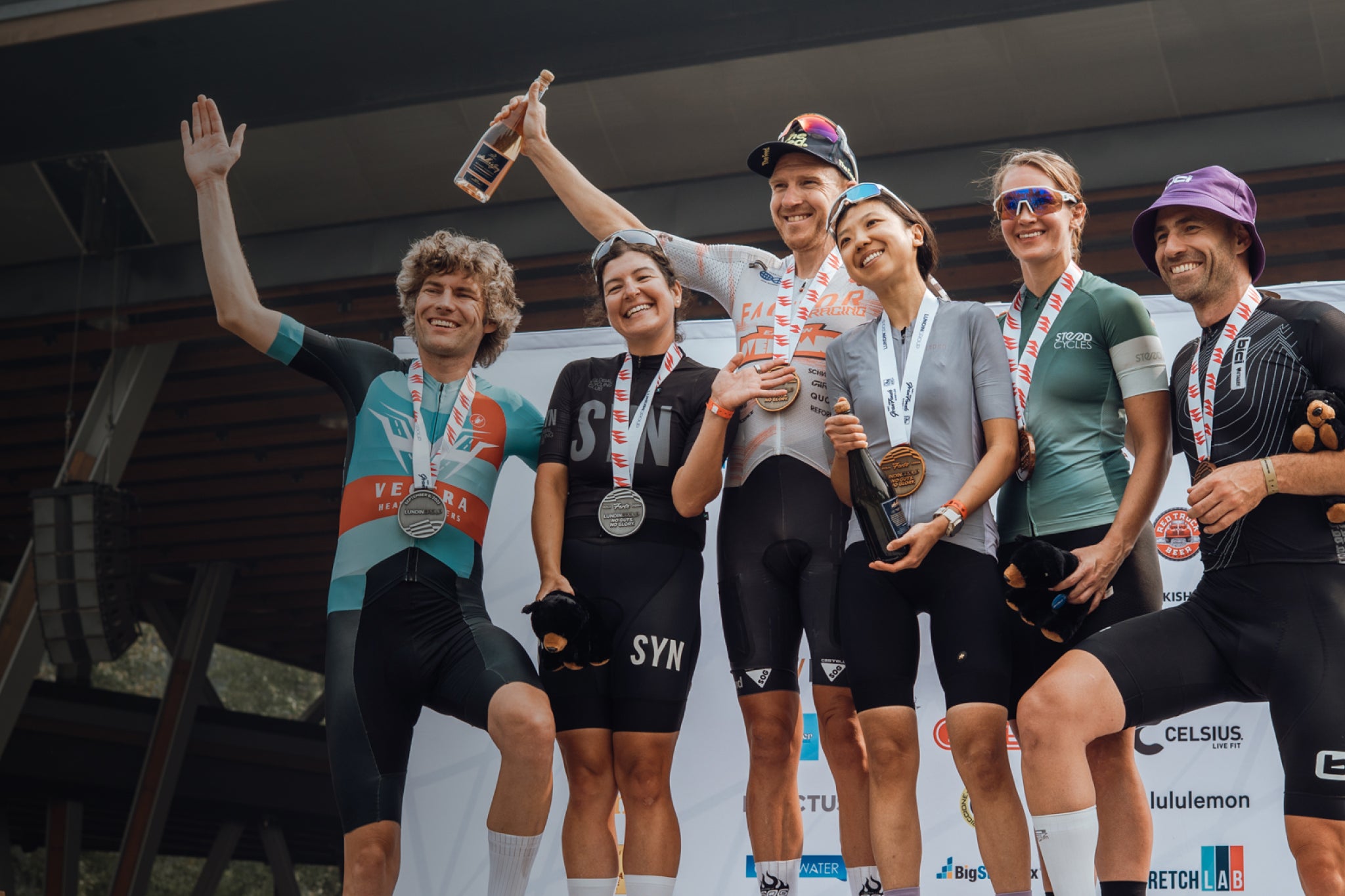 Group of cyclists celebrating on a podium with medals and bottles.