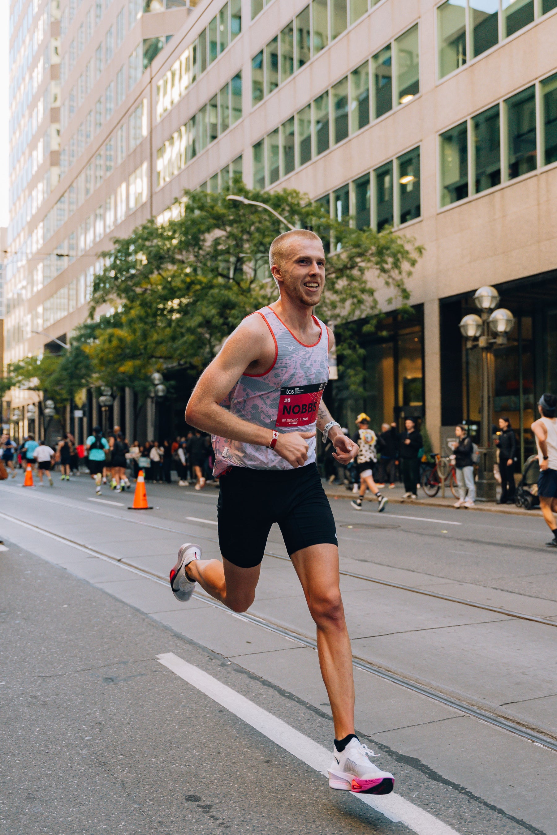 Man running on a city street with buildings and pedestrians in the background