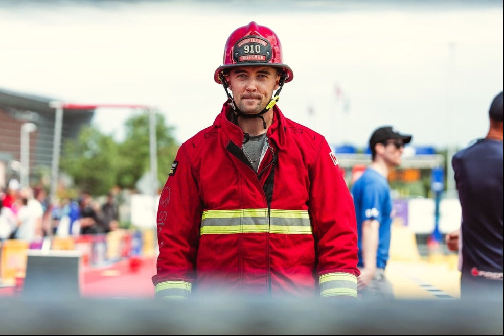 Firefighter in red uniform and helmet standing outdoors with blurred background