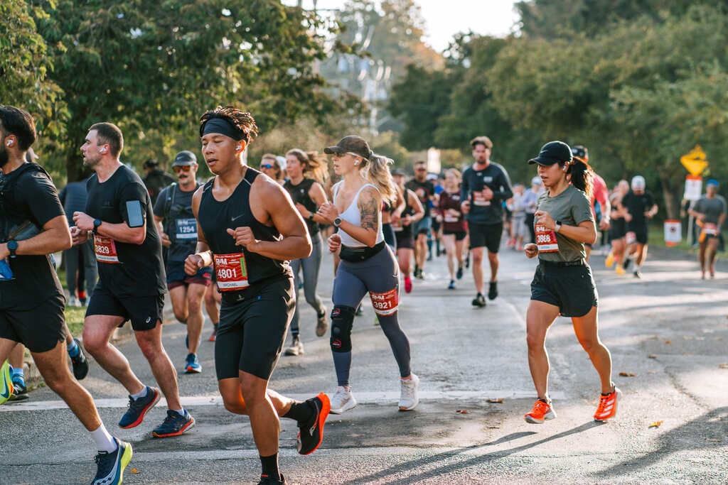 Runners participating in a race on a street with trees and buildings in the background.