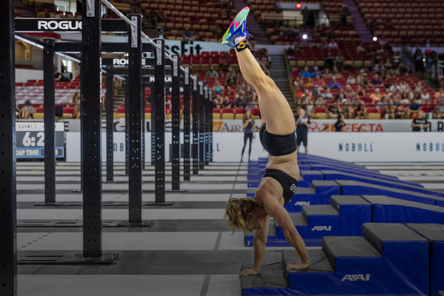 Person performing a handstand on blue boxes in a gymnasium with spectators in the background